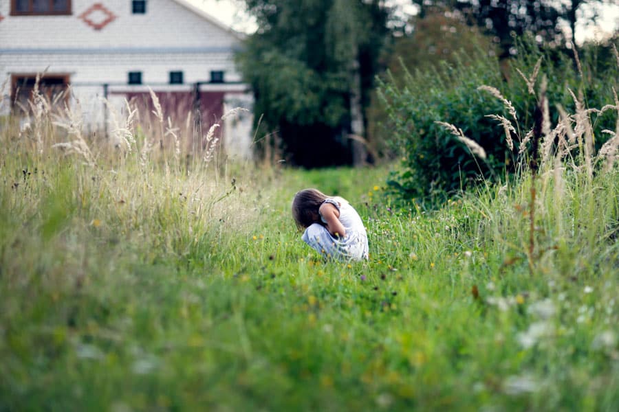 child squats in a semi wild garden looking bored