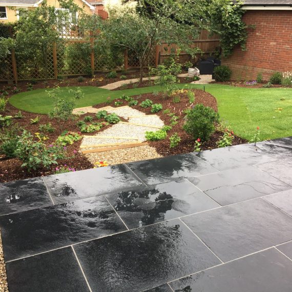 sloping garden with black basalt patio in the foreground and winding path leading through a lawn