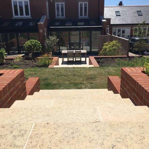 view from the top of a steeply sloping garden down towards a pretty patio and seating area