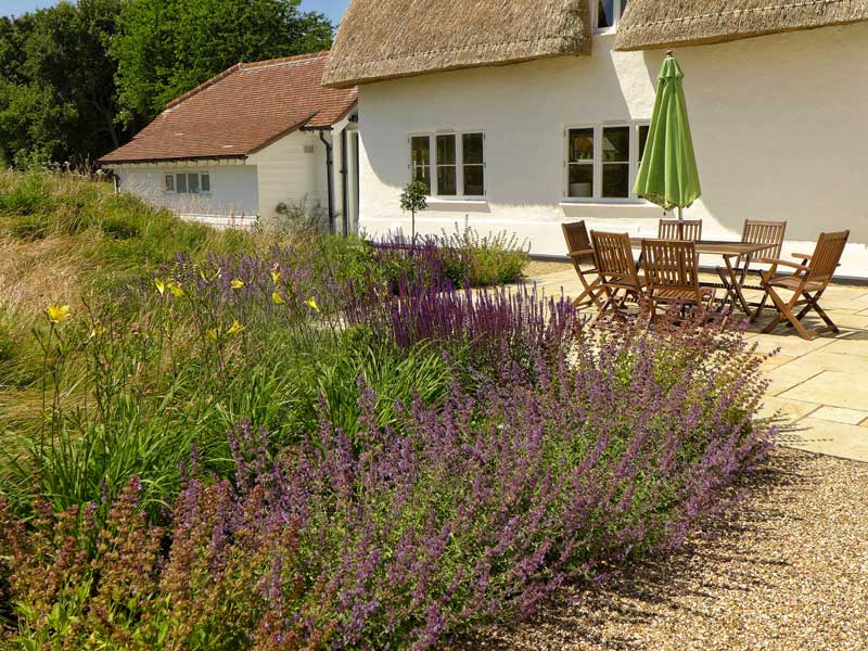 pretty thatched cottage with a generously sized patio hugged by banks of salvia and wildflowers