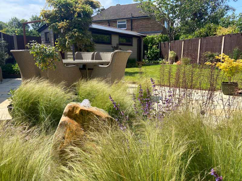 bespoke water feature made from a boulder rising up from a bed of ornamental grasses