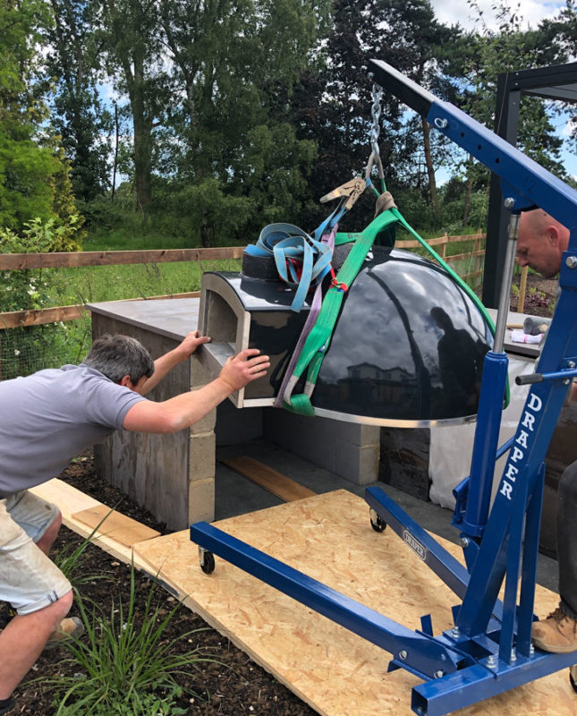 landscapers using lifting gear to install outdoor pizza oven