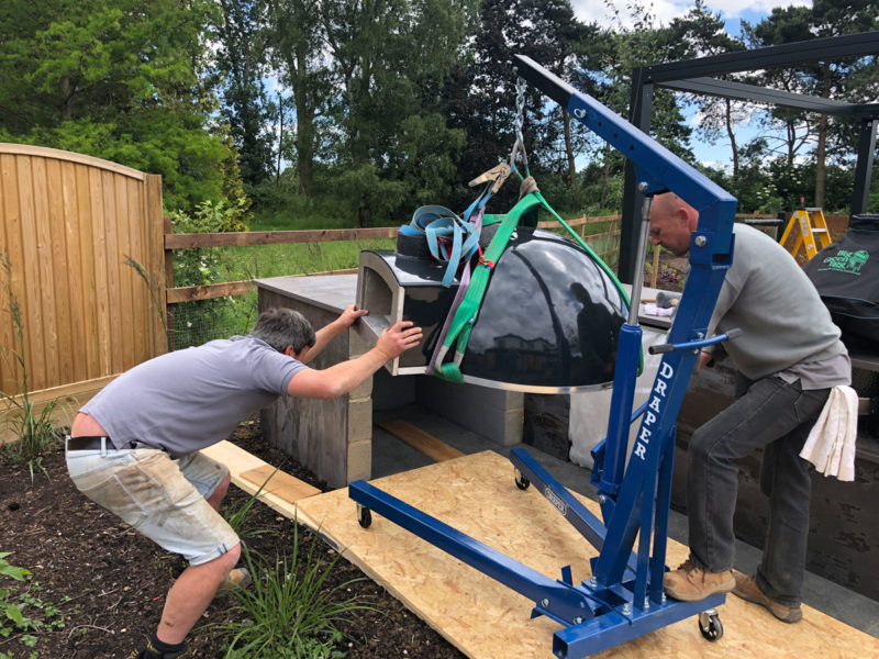 landscapers using lifting gear to install outdoor pizza oven