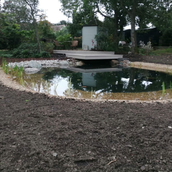 view of newly built wildlife pond and deck with soil in foreground prepared for sowing grass seed