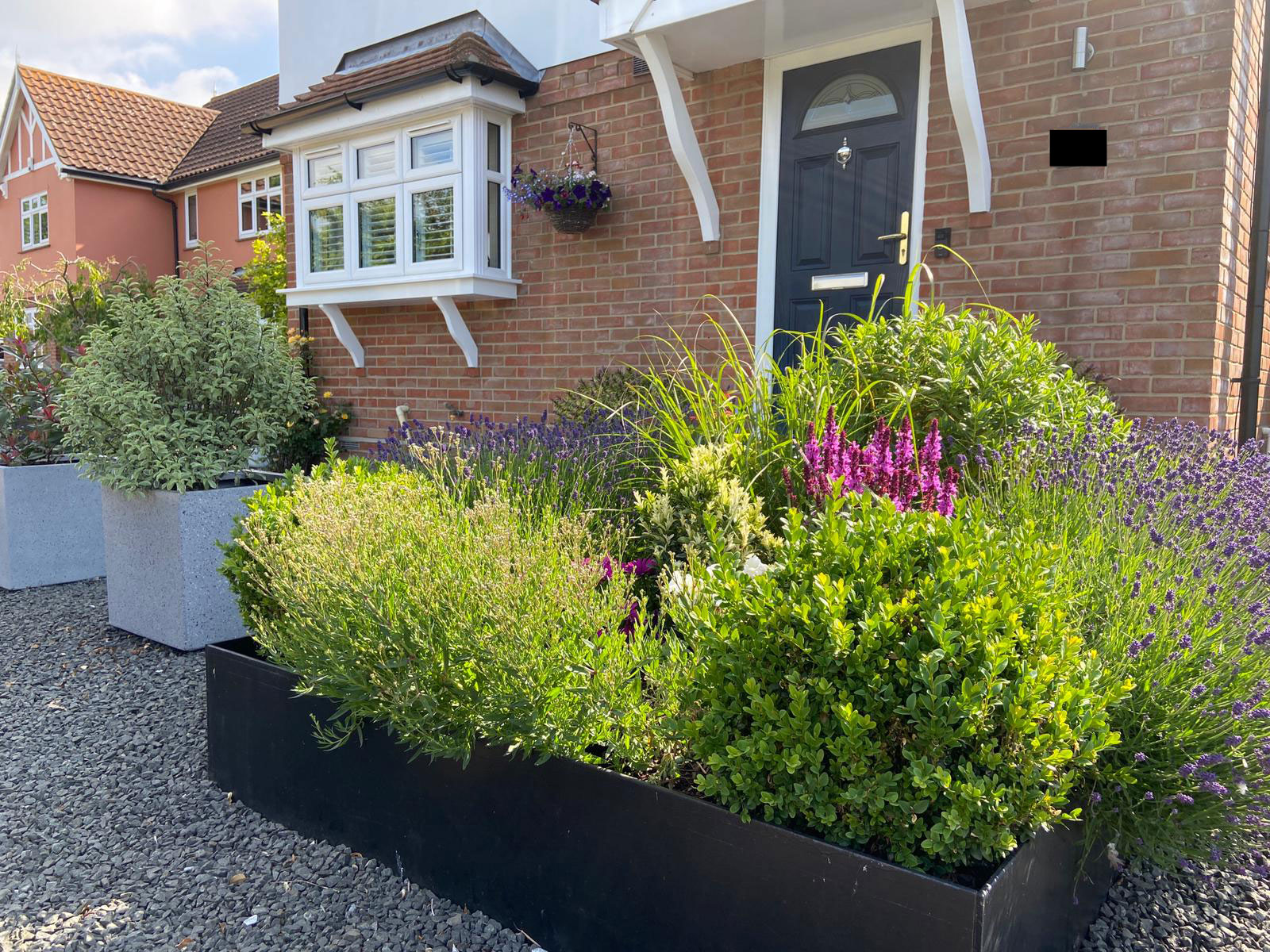 newbuild front garden with gravel surface and large planters full of shrubs and flowers