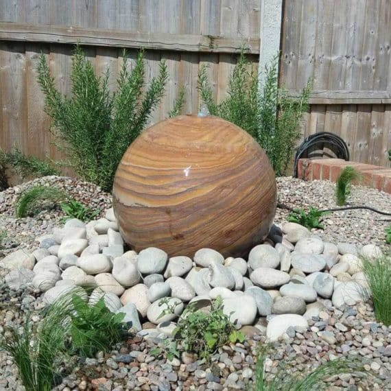 ball shaped stone water feature surrounded by pebbles