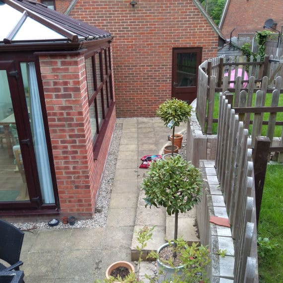 Before landscaping small garden terrace beside conservatory on left with high retaining wall and upper garden terrace to the right
