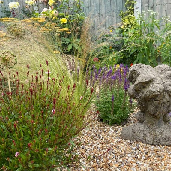 stone ornament in gravel garden surrounded by flowering plants and grasses