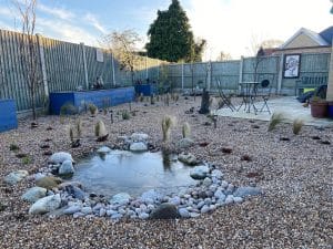 Pretty pond within a gravel garden. Pond is surrounded by pebbles along with young herbaceous plants