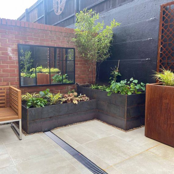 paved garden with plants in rectangular containers and an outdoor mirror to give the illusion of more space