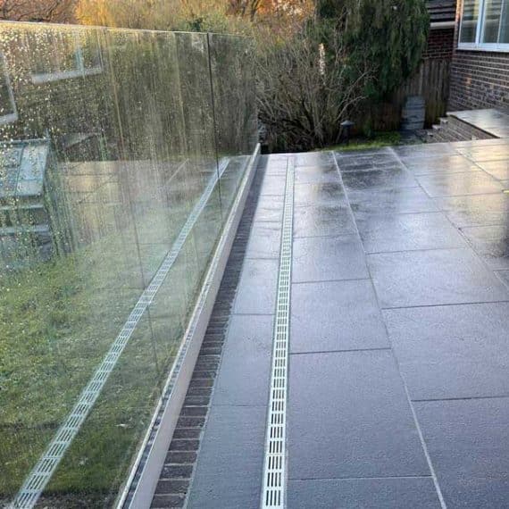striking black patio with silver slot drains and seamless glass balustrade to the left of the image
