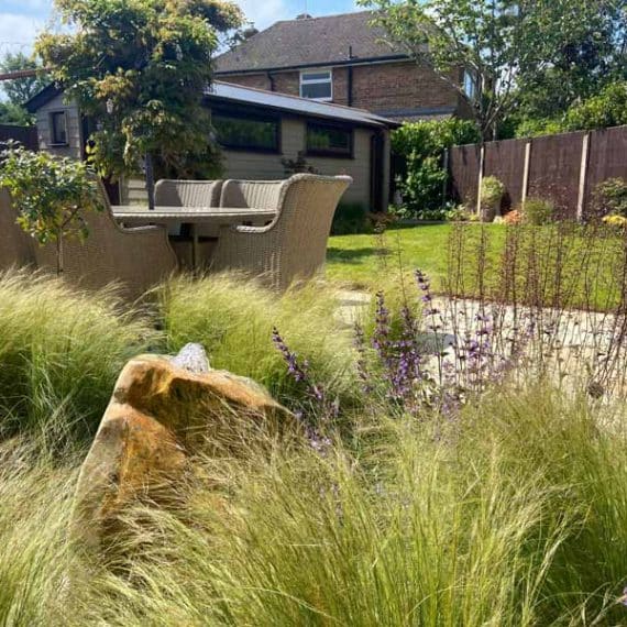 Water feature comprising large boulder with water bubbling from the top and surrounded by ornamental planting